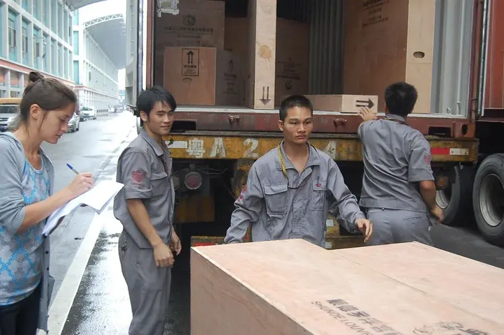 Shipment coordinator checking a list as workers prepare crated goods for loading into a container in China